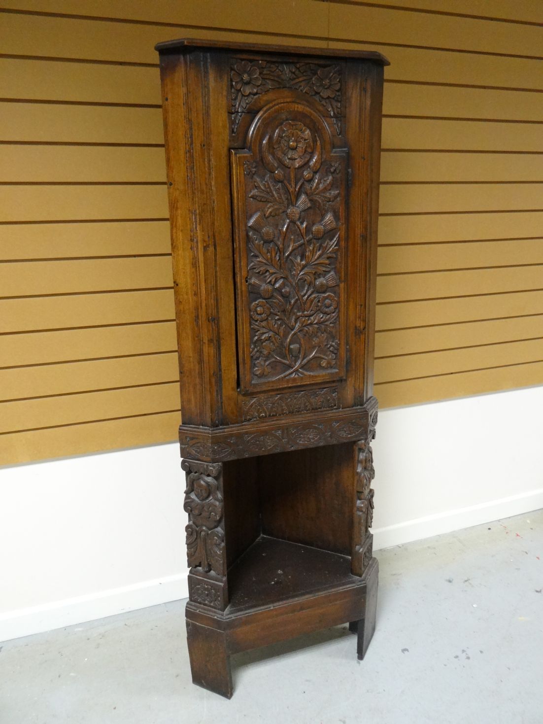 An early-twentieth century standing corner cupboard, profusely carved with figures, flowers and