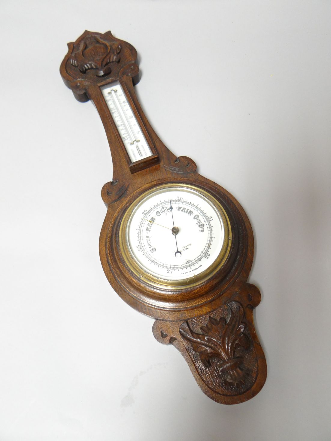 A carved dark oak encased banjo aneroid barometer, with printed dial and brass bezel, 25.5 ins