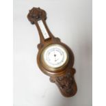 A carved dark oak encased banjo aneroid barometer, with printed dial and brass bezel, 25.5 ins