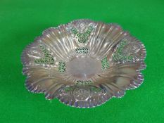 A circular-based pierced silver dish having a wavy border and fluting interspersed with floral and