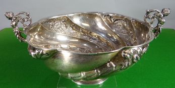 A high-Victorian silver footed bowl of swirling-form, floral embossed and with figural twin-handles,