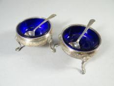 A pair of circular silver salts with Bristol-blue glass liners and on pad-feet with spoons, London