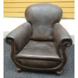 A brown leatherette studded club armchair on bun-feet with casters