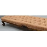 A Victorian walnut framed long foot-stool with buttoned stuff-over upholstery and carved frieze,