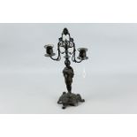 A cast bronze twin sconce candelabra of a young person semi-robed standing upon a three footed