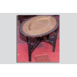 An Indian carved oval table and stand with dished oval brass tray, decorated with multi panels of