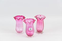 Set of three cranberry glass vases with fluted rims and plain bases, all with pontil marks, 17 cms