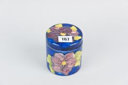 A Moorcroft pottery cylindrical pot and cover decorated in the clematis pattern on a cobalt blue