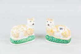 A pair of Staffordshire pottery models of recumbent cats opposing figures, with ochre colour