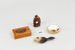 A horn round lidded box, a horn caddy spoon, a mauchline ware type box and a carved oriental netsuke