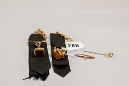 Two black cloth ribbons, each with a yellow metal swivel and pendant, each of the pendants with a