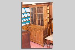 An early 19th Century Welsh oak type bookcase cupboard, the upper section having twin glazed doors