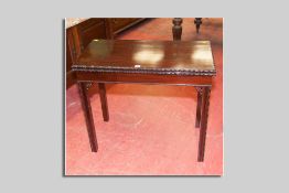 An Edwardian mahogany flip top card table with carved edge moulding, inverted chamfered legs with