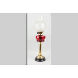 A brass based oil lamp with cranberry glass reservoir and etched bowl shade