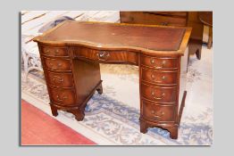 A neat reproduction mahogany serpentine front kneehole desk with tooled leather top having a