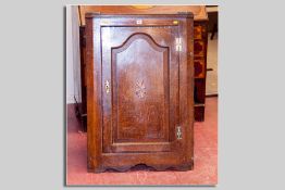 An antique oak single door hanging cupboard having a sunburst inlay and with a shaped and field