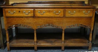 An oak dresser base with open plank shelf, pierced apron to four baluster supports and with three