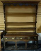 A dark oak dresser with open shelved and boarded base, three drawers and closed rack, circa 1830,