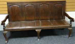 An oak settle with four fielded panels to the slightly angled back and four recesses to the seat,