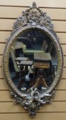 An oval gilt wood framed mirror with candle sconces and being decoratively carved in the Rococo