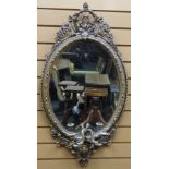 An oval gilt wood framed mirror with candle sconces and being decoratively carved in the Rococo