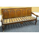 An oak settle, with slanted back having four fielded panels and with pine slats to the seat, circa