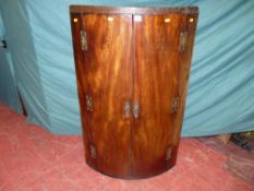 A Georgian mahogany bow front hanging wall cupboard with brass 'H' hinges and escutcheons, the