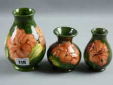 Three Moorcroft pottery green ground 'Hibiscus' small vases, one 15 cms and the other two 10 cms