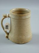 A St Ives pottery tankard in oatmeal glaze, ribbed body and scroll handle, 12.5 cms high