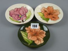 Three Moorcroft pin dishes - Magnolia on a cream ground, Hibiscus on a cream ground and Hibiscus