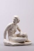 Skulptur. Weiß glasiertes Steingut. Sitzender, weiblicher Akt auf ovalem Natursockel. H: 30 x 30 cm.