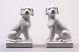 Paar Buchstützen. Böhmen, um 1920. Fayence, weiß glasiert. Sitzende Hunde auf rechteckigem Sockel.