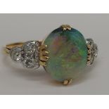 A ladies dress ring having a large opal in a claw setting with trio of diamonds to each shoulder