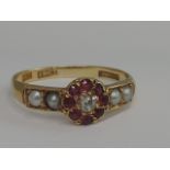 A ladies diamond and ruby cluster ring having seed pearl decoration to shoulders on a yellow metal