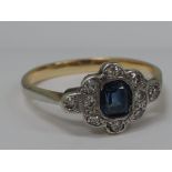 A ladies dress ring having a baguette cut sapphire in a diamond surround on a yellow metal loop,