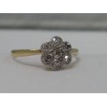 A ladies diamond daisy cluster ring having a milligrain setting on a yellow metal loop stamped 18