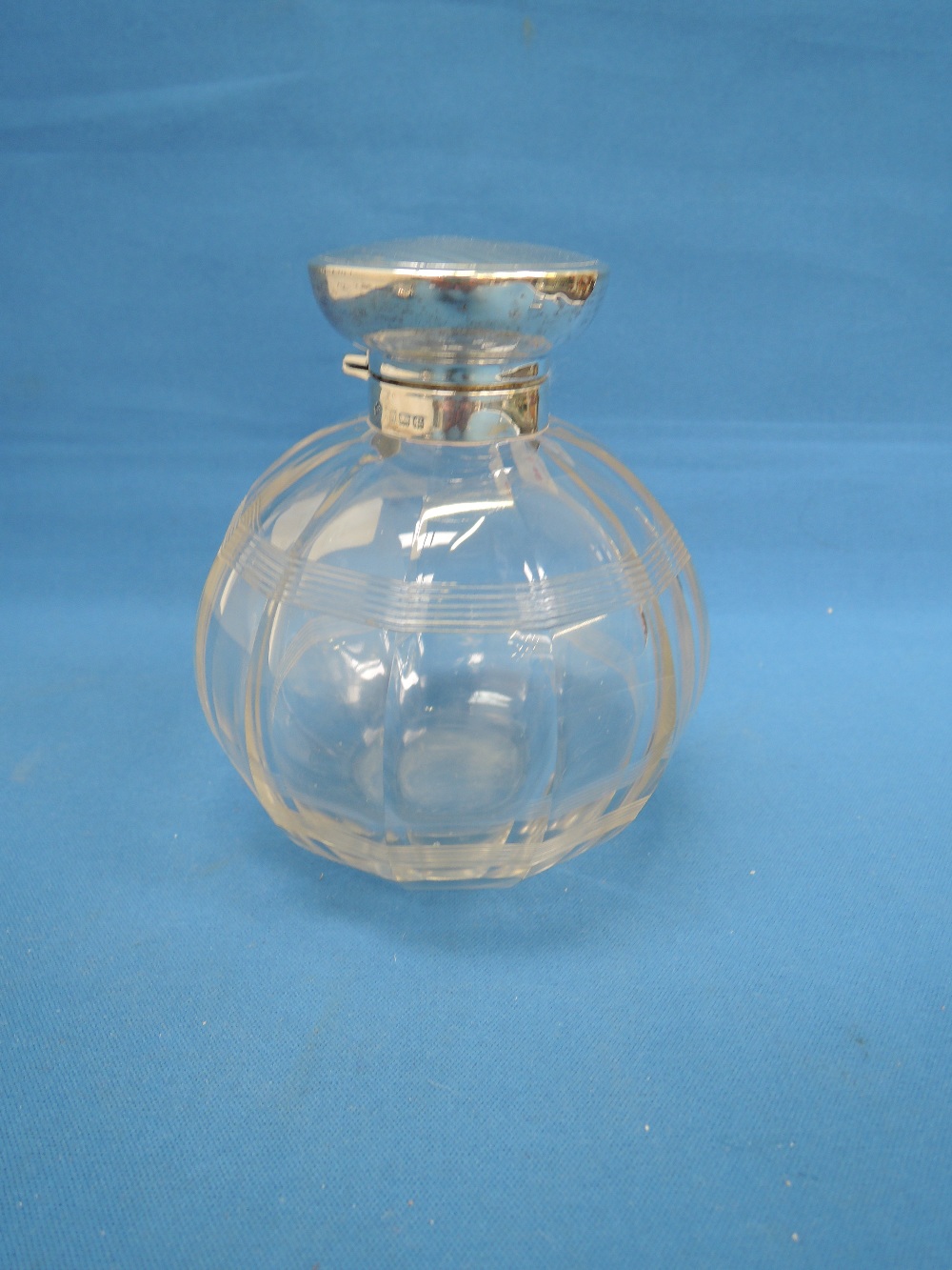 A glass perfume bottle of facetted spherical form having a silver collar and lid with engine
