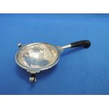 A white metal tea strainer of traditional form having an ebonised handle, no marks but tested as