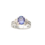 A diamond and tanzanite ring, composed of an oval mixed-cut tanzanite between princess-cut and round