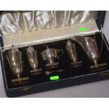 A cased silver five piece condiment set comprising caster, pepperettes, mustard (with blue glass