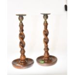 A pair of oak candlesticks with brass sconces, barley twist stems and circular bases.