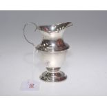A George V silver cream jug, Chester 1911, of baluster form on a stepped circular foot.
