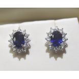 A pair of sapphire and diamond earrings, four claw set within a bezel of diamonds. Mounted in 18ct