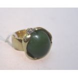 A gold ring set with an imposing jade cabochon, the mount set with two diamonds, (unmarked but tests