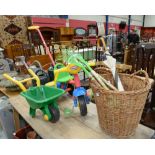 A childs push along trike, a child's wheel barrow, wicker basket, childrens garden tools and a