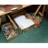 Two boxes inc. a quantity of costume jewellery, table linens and a wicker bound wine bottle