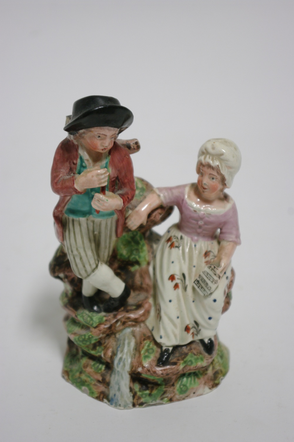 An early 19th century Staffordshire pottery group of male & female musicians, he playing a pipe, she