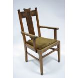 An Arts & Crafts style oak elbow chair by Jas. Schoolbred & Co., with carved stylised foliate