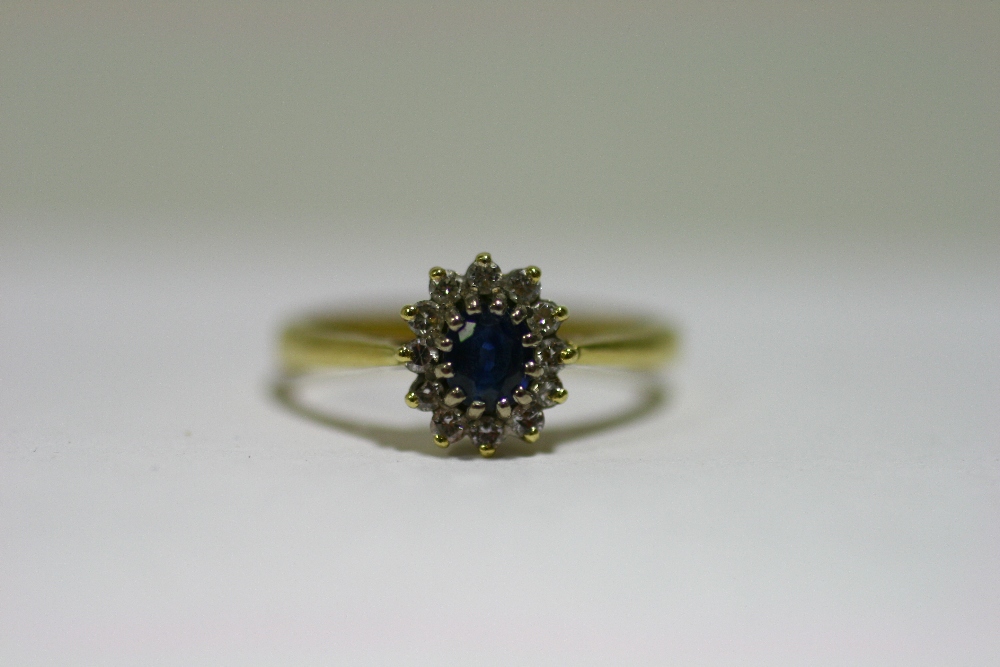 A sapphire & diamond ring, the oval sapphire set within a border of twelve small diamonds, to an