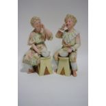 A pair of late 19th century German painted bisque male & female seated costume figures, each blowing